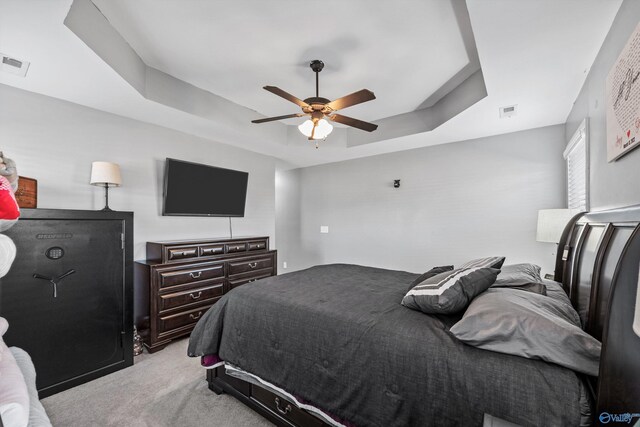 bedroom with a raised ceiling, visible vents, ceiling fan, and light carpet