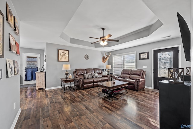 living room featuring a raised ceiling, a ceiling fan, and baseboards
