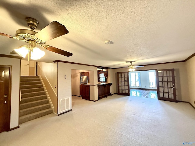 unfurnished living room with ceiling fan, french doors, a textured ceiling, and ornamental molding