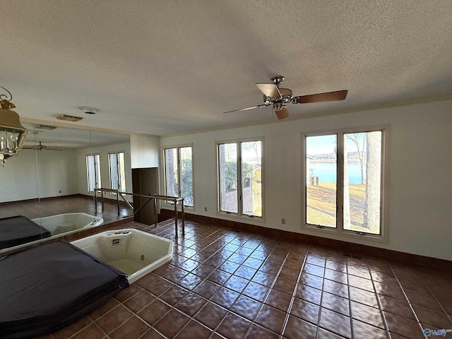 interior space with a textured ceiling, ceiling fan, a water view, and dark tile patterned floors