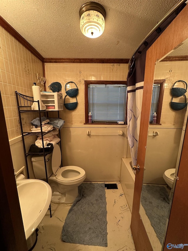 bathroom with a textured ceiling, toilet, a sink, ornamental molding, and shower / bath combination with curtain