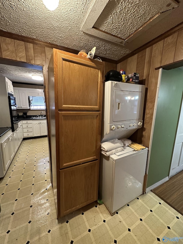 laundry area with a textured ceiling, stacked washer and dryer, laundry area, a sink, and light floors