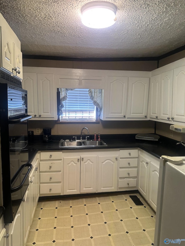 kitchen with dark countertops, white cabinets, a sink, and light floors