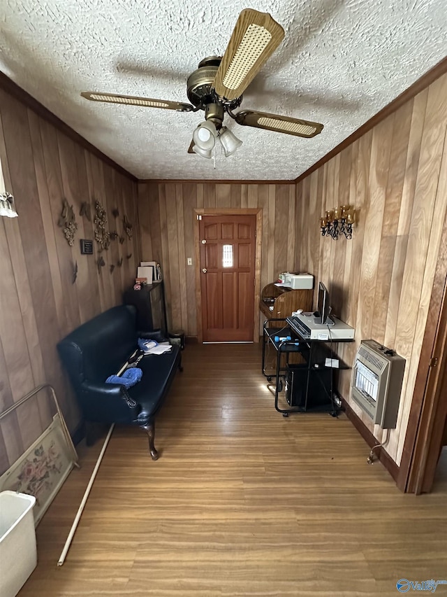 sitting room featuring a textured ceiling, wood finished floors, a ceiling fan, ornamental molding, and heating unit