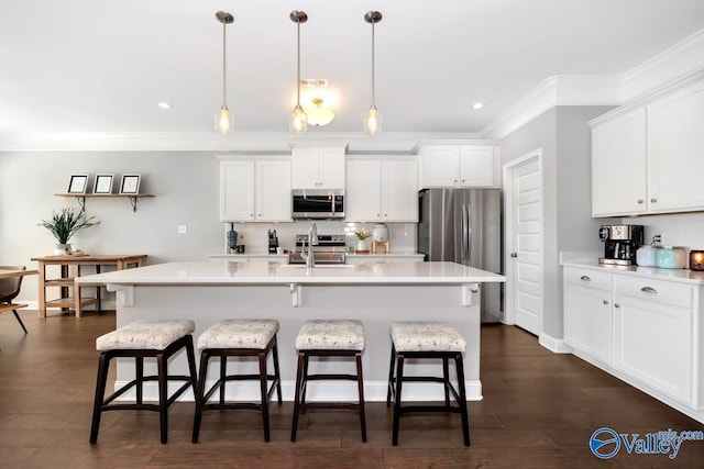 kitchen with an island with sink, appliances with stainless steel finishes, decorative light fixtures, light countertops, and white cabinetry