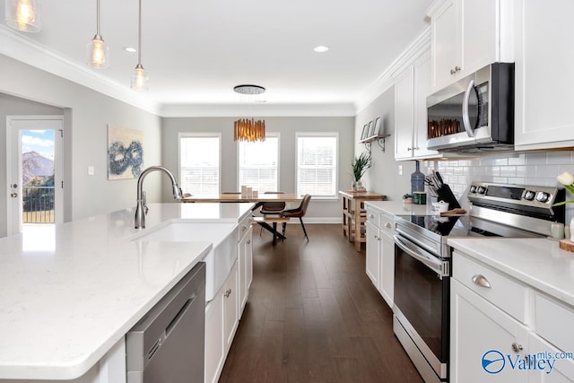 kitchen with appliances with stainless steel finishes, white cabinets, decorative light fixtures, and an island with sink