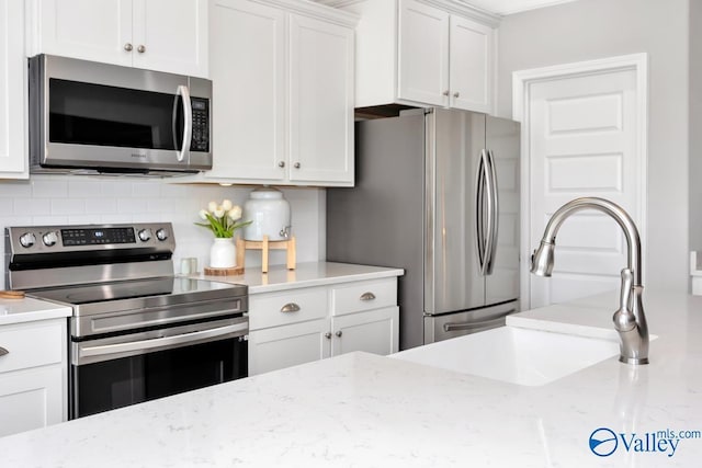 kitchen featuring appliances with stainless steel finishes, decorative backsplash, light stone countertops, and white cabinets