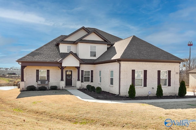 view of front of home with a shingled roof, brick siding, and a front lawn