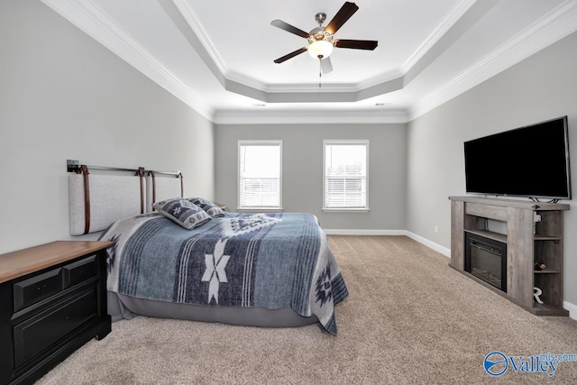 bedroom featuring light carpet, ornamental molding, a raised ceiling, and a glass covered fireplace