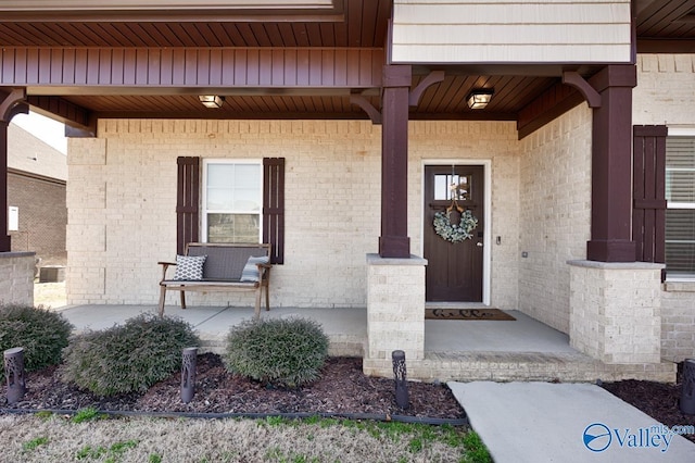 view of exterior entry with a porch and brick siding