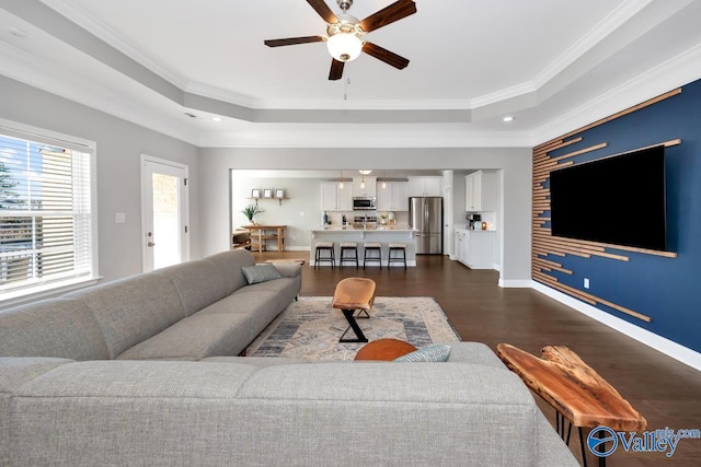 living room featuring dark wood-style floors, a tray ceiling, crown molding, and baseboards