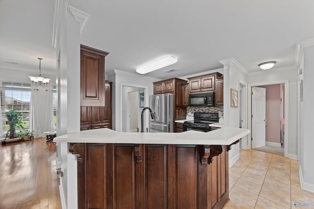kitchen featuring crown molding, light countertops, a kitchen breakfast bar, decorative backsplash, and black appliances