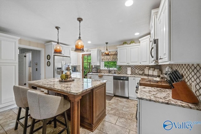 kitchen featuring light stone countertops, white cabinetry, a kitchen island, tasteful backsplash, and appliances with stainless steel finishes
