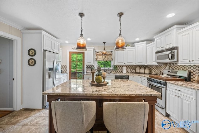 kitchen with a center island, light stone counters, white cabinetry, stainless steel appliances, and tasteful backsplash