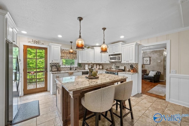 kitchen featuring crown molding, appliances with stainless steel finishes, a decorative wall, and white cabinetry