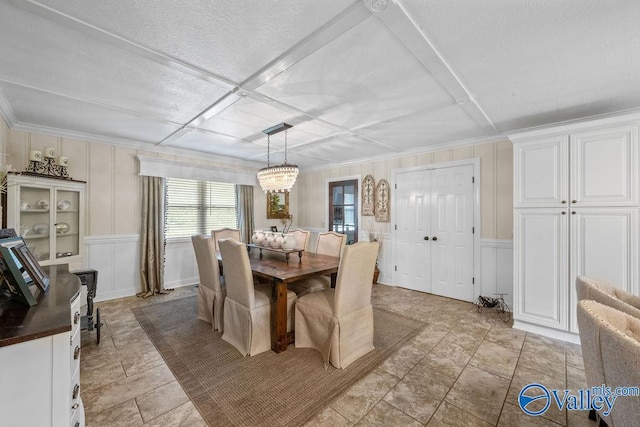 dining space with an inviting chandelier, a decorative wall, wainscoting, and stone finish floor