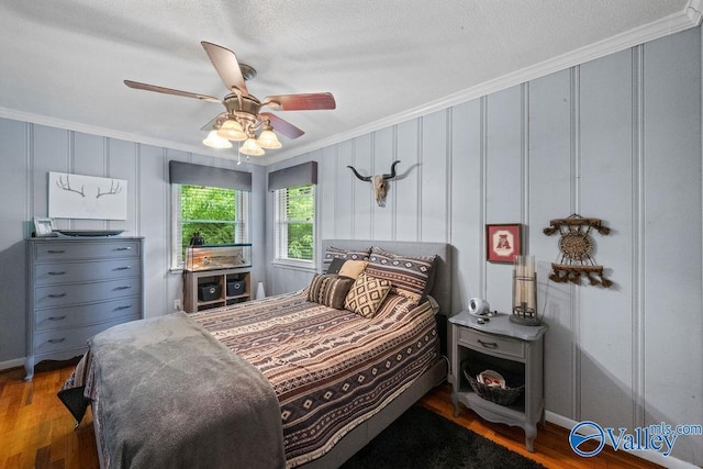bedroom featuring a decorative wall, wood finished floors, ornamental molding, ceiling fan, and baseboards