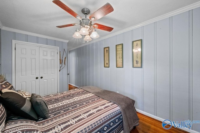 bedroom with a ceiling fan, a closet, a decorative wall, crown molding, and wood finished floors