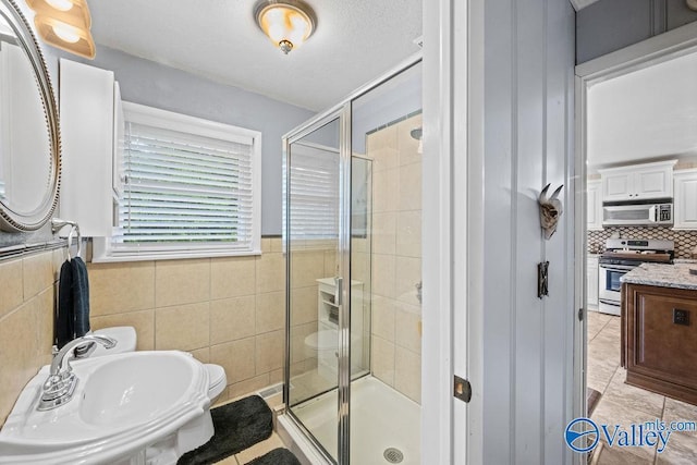 bathroom with a stall shower, tile walls, tile patterned flooring, and a sink
