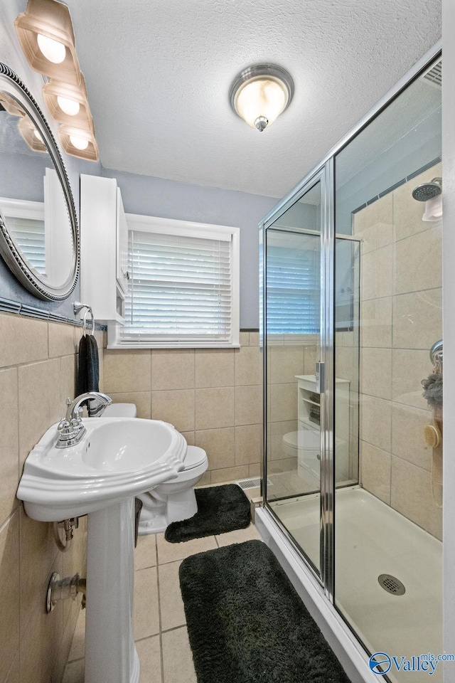 full bath featuring a shower stall, tile walls, tile patterned floors, and a textured ceiling