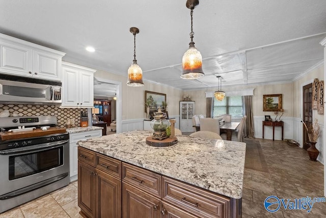 kitchen with white cabinets, appliances with stainless steel finishes, a kitchen island, and light stone countertops