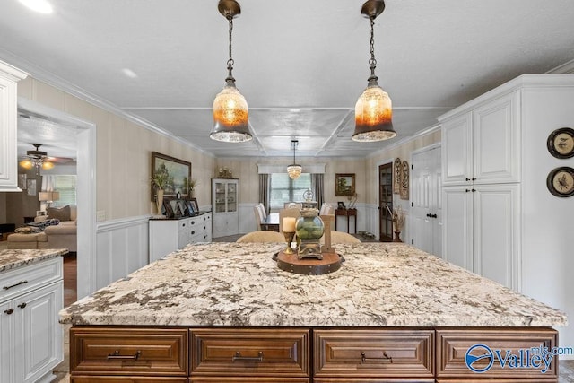 kitchen with light stone counters, white cabinetry, a kitchen island, and a decorative wall