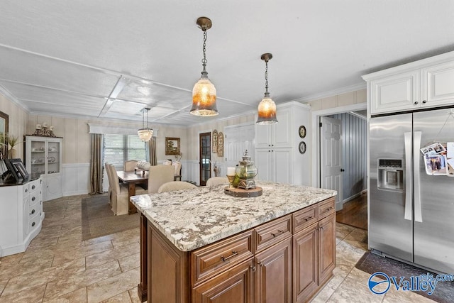 kitchen with decorative light fixtures, light stone counters, stainless steel fridge, white cabinets, and a kitchen island