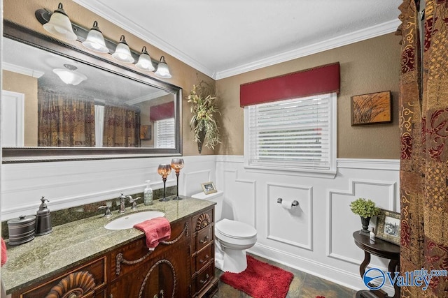 bathroom featuring toilet, a wainscoted wall, crown molding, a decorative wall, and vanity