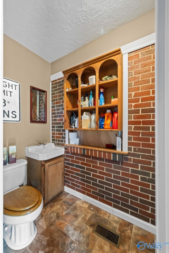 bathroom featuring toilet, stone finish flooring, a sink, a textured ceiling, and visible vents