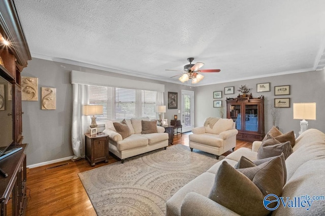 living area featuring light wood-type flooring, visible vents, ceiling fan, crown molding, and baseboards