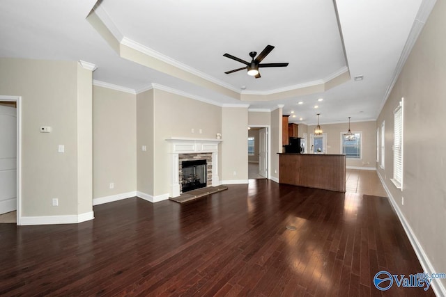 unfurnished living room with ceiling fan, a tray ceiling, a stone fireplace, and dark hardwood / wood-style flooring