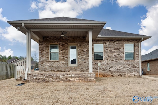 back of property with brick siding, roof with shingles, fence, and a ceiling fan