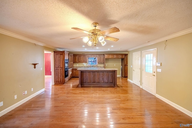 kitchen with a center island, crown molding, light wood finished floors, baseboards, and ceiling fan