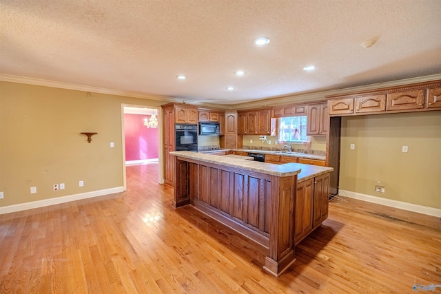 kitchen with a sink, black appliances, crown molding, light wood-type flooring, and a center island