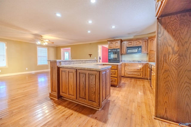 kitchen featuring a center island, crown molding, black microwave, light countertops, and light wood-style flooring
