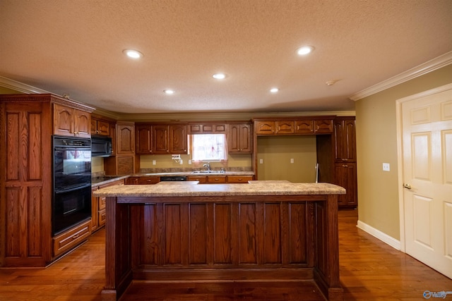 kitchen featuring a center island, crown molding, dark wood finished floors, black appliances, and a sink