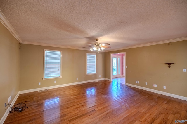 empty room with a ceiling fan, visible vents, wood finished floors, baseboards, and ornamental molding