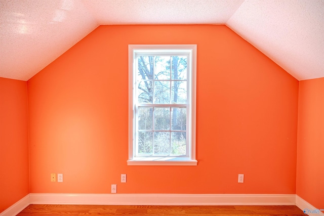 bonus room with a textured ceiling, lofted ceiling, baseboards, and wood finished floors
