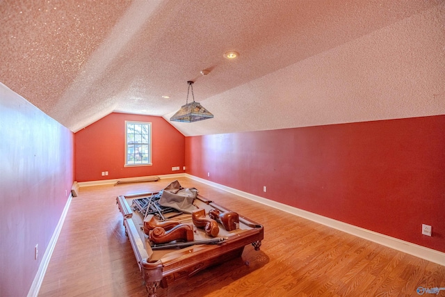 additional living space with vaulted ceiling, wood finished floors, baseboards, and a textured ceiling