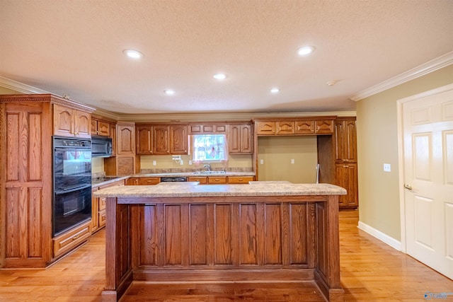 kitchen with light wood finished floors, a center island, ornamental molding, black appliances, and a sink