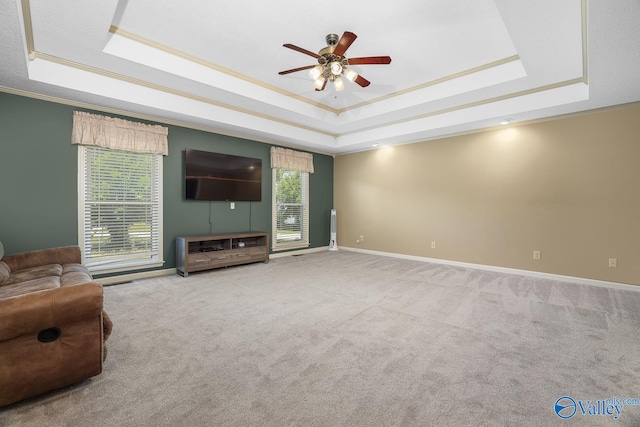 unfurnished living room featuring a ceiling fan, a raised ceiling, crown molding, and carpet