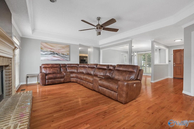 living room featuring crown molding, a raised ceiling, a brick fireplace, and a ceiling fan