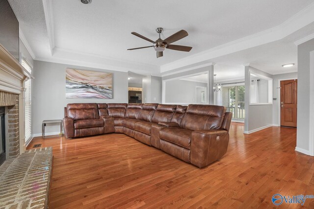 living room with crown molding, light wood-type flooring, ceiling fan, a fireplace, and a raised ceiling