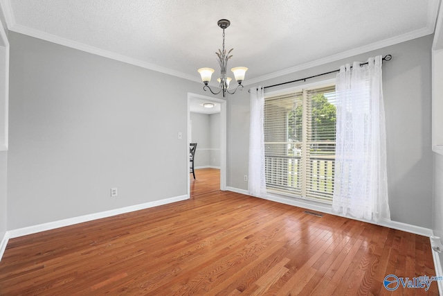 spare room with ornamental molding, a chandelier, visible vents, and wood finished floors