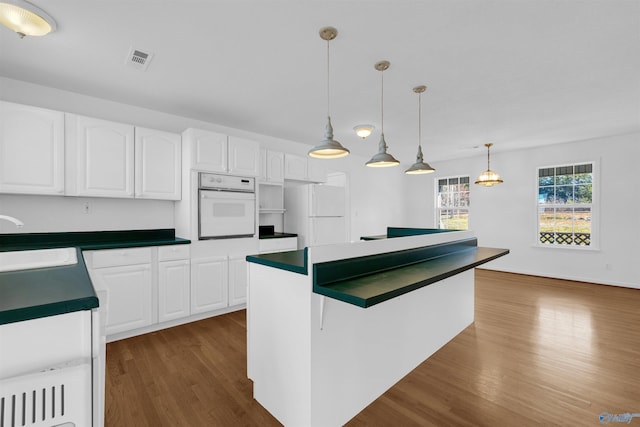 kitchen featuring pendant lighting, sink, white cabinets, white appliances, and dark hardwood / wood-style floors