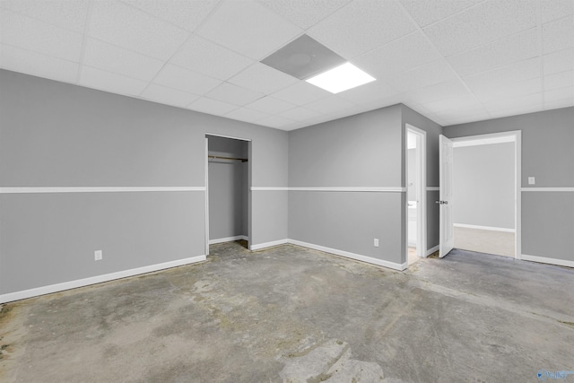 unfurnished bedroom with concrete floors, a paneled ceiling, and a closet