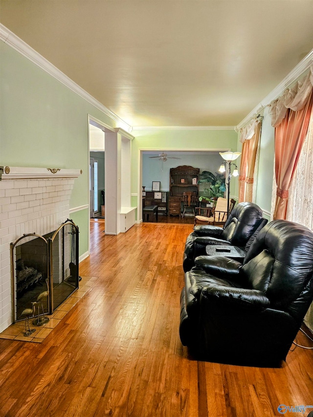 living room featuring a brick fireplace, wood-type flooring, ceiling fan, and crown molding