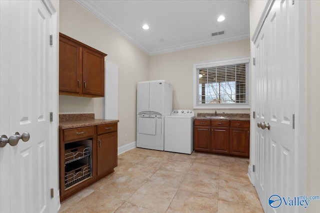 clothes washing area with cabinets, sink, ornamental molding, and washing machine and dryer