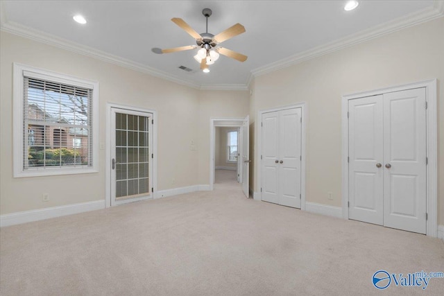 unfurnished bedroom with ceiling fan, light carpet, crown molding, and two closets