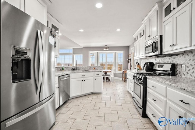 kitchen featuring white cabinets, glass insert cabinets, appliances with stainless steel finishes, a sink, and backsplash